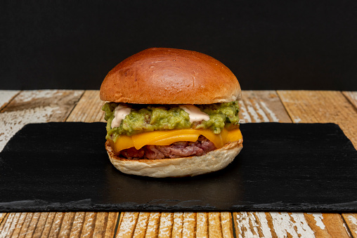 A delicious double cheddar beef patty with lots of guacamole and mayonnaise on top of the meat on a lightly toasted bun