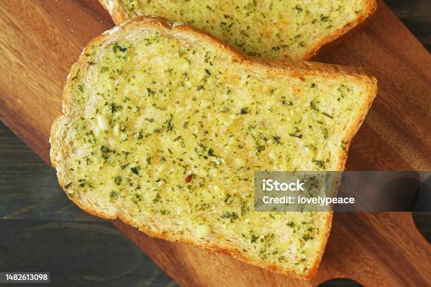 Closeup Of Delectable Freshly Cooked Homemade Garlic Butter Toast On Wooden Breadboard Stock Photo - Download Image Now