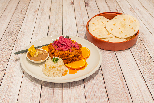 Cochinita pibil stew with rice and chipotle with purple onion and container with corn tortillas for tacos on white table