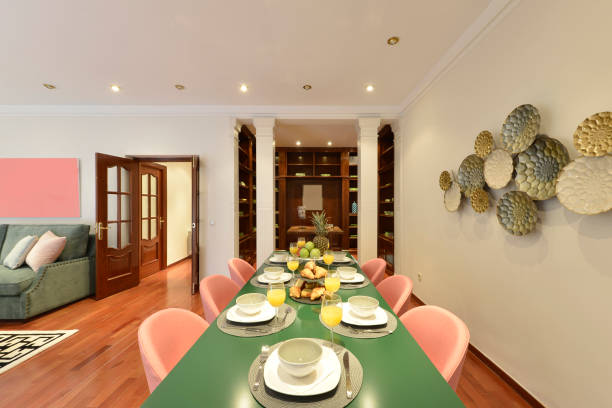 Long plain green dining table with pink velvet upholstered chairs in a living room with sofas and an office with classic wooden bookcase
