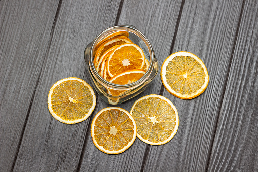 Dry orange slices on the table and in a jar. Flat lay. Copy space. Dark wooden background.