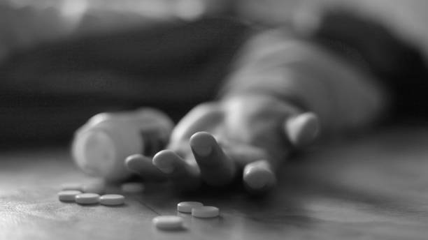 Man lying on the floor, unconscious or dead due to drugs abuse, focus on fingers with pills stock photo