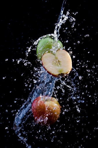 close up of fresh colorful apples and a sliced apple with splashing water in front of a black background