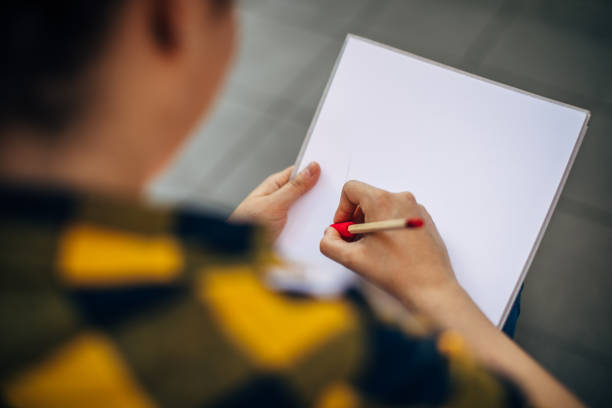 Hands of a young woman who is drawing on the sketching pad with colored pencil