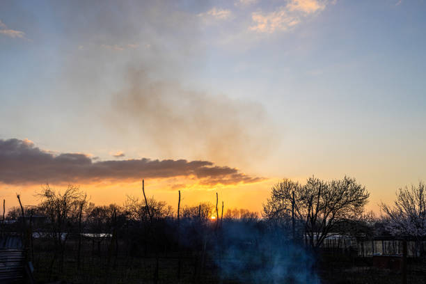 sunset sky over rural gardens with smoke from campfires in spring evening