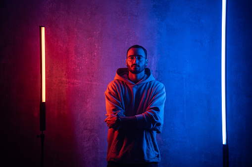 Portrait of a handsome modern man standing in front of the wall between neon lights in studio.