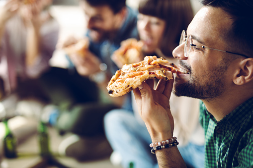 Close up of young man enjoying while eating pizza with his friends