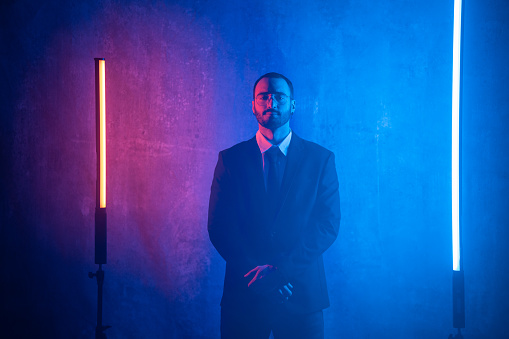 Portrait of a handsome businessman in suit standing in front of the wall between neon lights in studio.