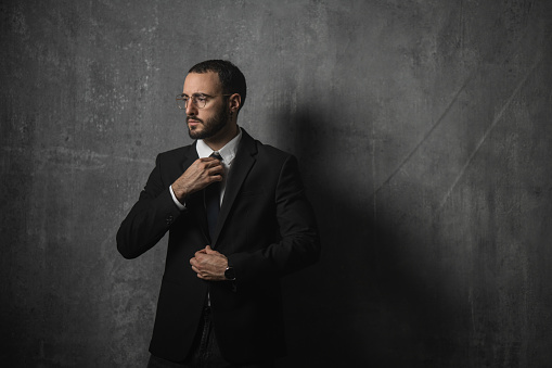 Portrait of a handsome businessman in suit standing in front of the wall in studio.