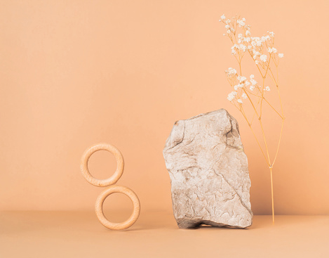 Creative stone podium with dry flower and a wooden rings for cosmetics or products on a beige background. Marketing scene mockup. Wabi sabi trend