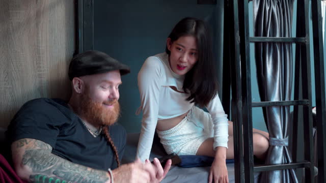 Lifestyles couple tourists backpacker traveling concept, Caucasian man with beard and tattoo and cheerful Asian woman spend time together using smartphone searching map guides planning for a trip