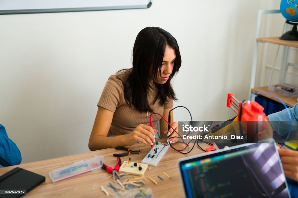 Teen smart student making a breadboard during a robotics course Latin young girl smiling while learning using an electronic breadboard in the robots class at the junior high school 3D Printing Stock Photo