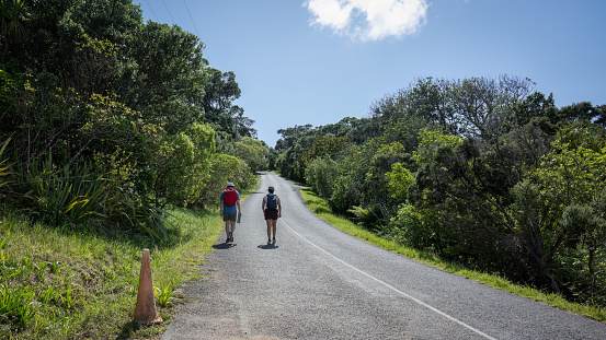Two people walking on asphalt road on hot summer day. Waiheke Island.