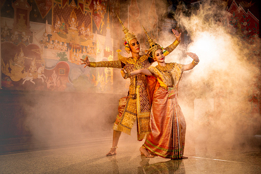 Pantomime (Khon) or traditional Thai classic masked play enacting scenes from the Ramakien (Ramayana) man dance with woman with a background of Thai paintings in a public place.