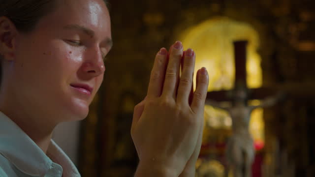 Young woman at prayer service prays in shrine of the Lord. Crucified Jesus Christ on the background. Close-up religious girl face in temple worshiping God.