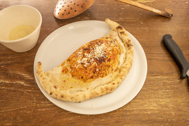 популярный рецепт итальянского кальцоне, фаршированного на камне и посыпанного тертым сыром пармезан на деревянном столе - pizza pastry crust stuffed cheese стоковые фото и изображения