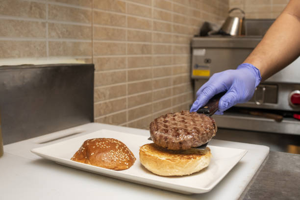 istock Gloved chef's hand assembling a hamburger with a good piece of beef meat cooked on the grill 1482640880