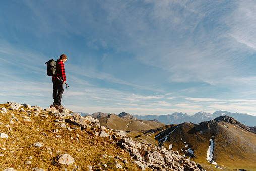 male hiker with red clothes, backpack, and trekking poles contemplates the mountain scenery from a mountain peak on a sunny day. lonely man. sport, travel and adventure.