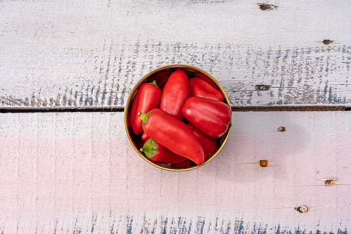 Top view photography of handful of small red bell peppers on pastel painted wood and metal nails