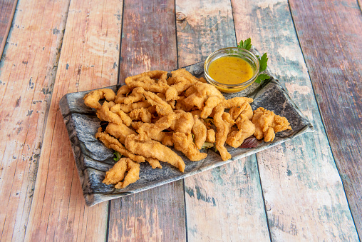 Tray of crispy chicken strips battered and fried in olive oil with sweet curry sauce on wooden table