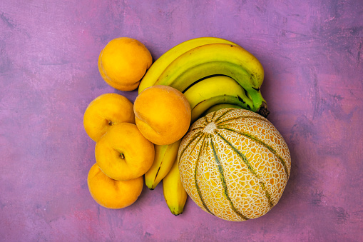 Small Gaul melon with bunch of bananas and yellow peaches on pink background