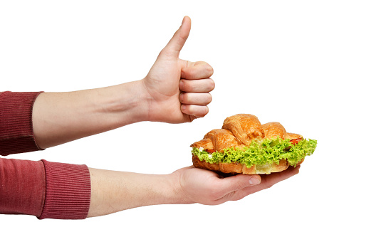 Sandwich croissant with salad is held in hands and show thumbs up. Man satisfied with taste and quality of croissant fast food street food.