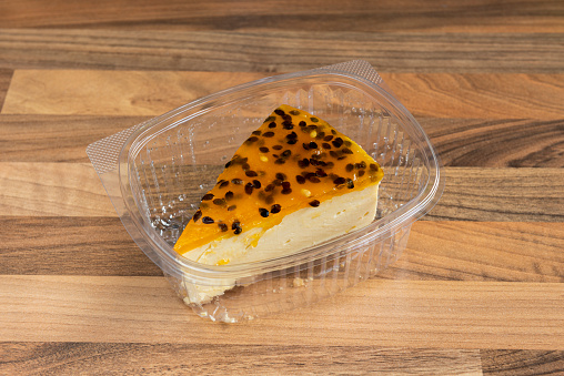 Portion of passion fruit cheesecake inside container for home delivery