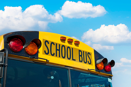 A close up photograph of the top corner of the front of a yellow school bus.