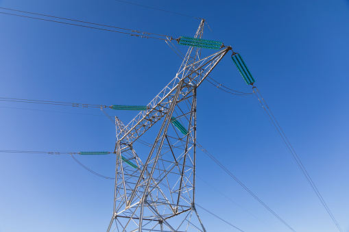 Close up on the top section of a high voltage transmission  pylon with power lines against a blue sky