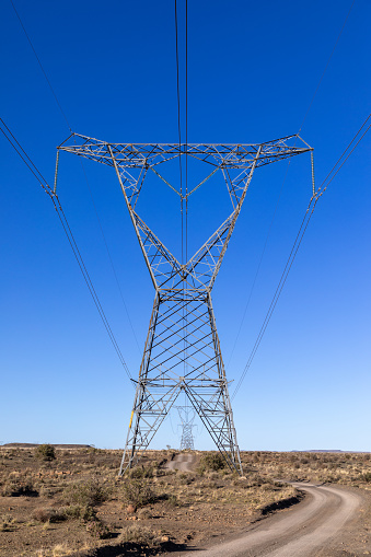 High voltage electricity transmission pylons with a two track gravel road running beneath it in an arid area.