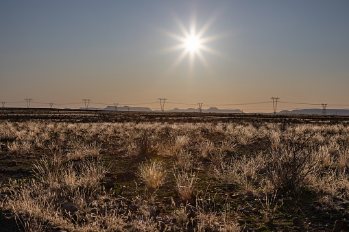 Karoo landscape in South Africa in the afternoon with the setting sun in the sky and high voltage electricity transmission lines in the distance.