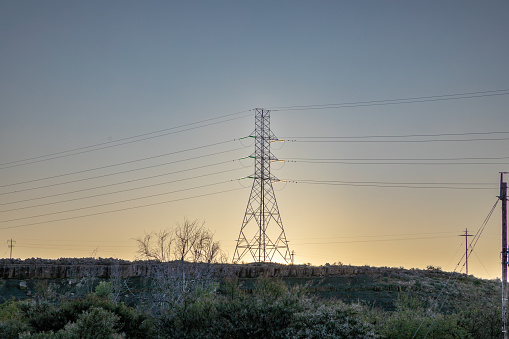 High-voltage power lines on a hill at sunset with the sun setting behind the pylon, high voltage electric transmission tower in the Karoo region of South Africa.