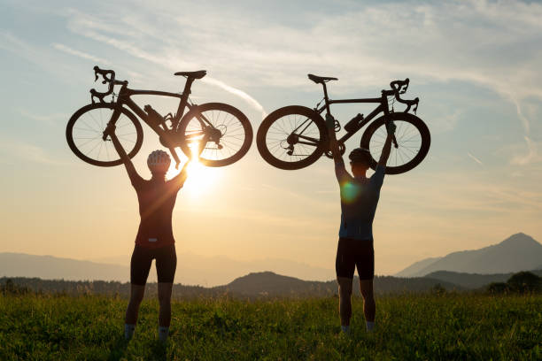 istock Two silhouettes holding bicycles high above heads, in winner pose 1482651180