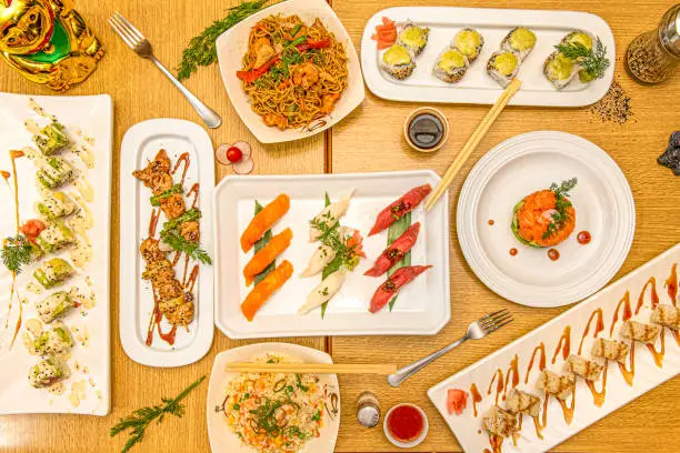 set of dishes of chinese food and sushi. salmon and avocado tartare, yakitori chicken skewers, butterfish nigiri, salmon and red tuna, tres delicias rice, uramaki and california roll