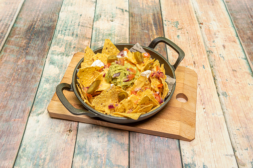 Cast iron pie pan with serving of Mexican corn nachos with guacamole, chopped red onion, sliced jalapenos, cheddar cheese and cream cheese