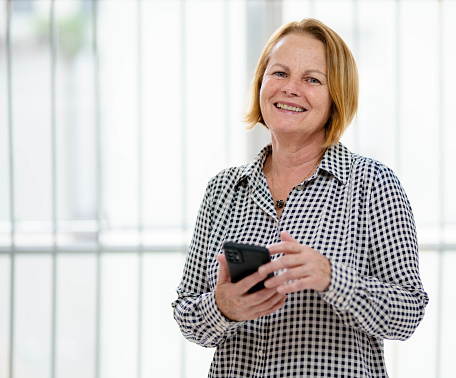 Portrait of a mature businesswoman smiling while standing with her mobile phone in a bright office
