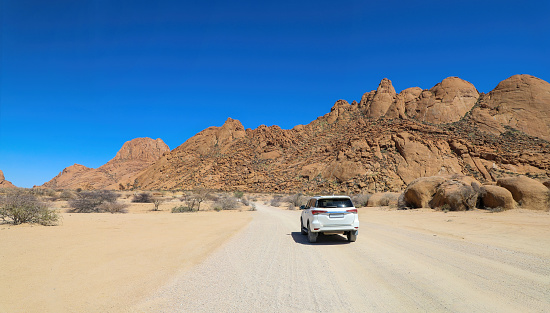 Lone white four wheel drive vehicle in the barren desert landscape of Spitzkoppe in Namibia