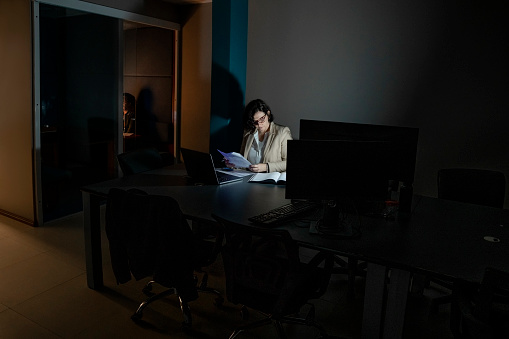 Mature businesswoman looking at documents while working late on a laptop computer in office