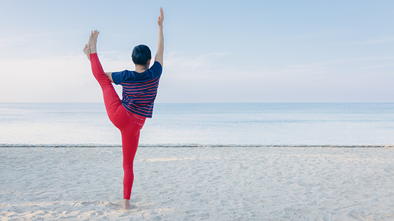 Strong Asia senior elder woman practicing yoga on the beach in summer morning with beautiful blue sky. Healthy lifestyle and fitness leisure concept.