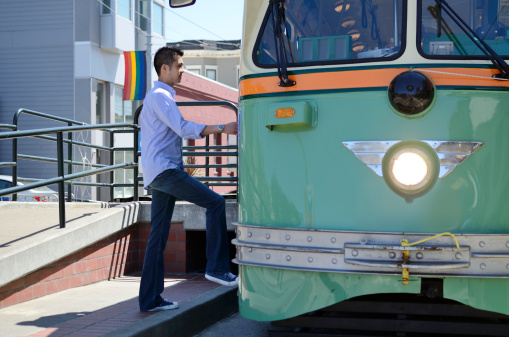 Young Asian man wearing a shirt and jeans steps up onto a tram car