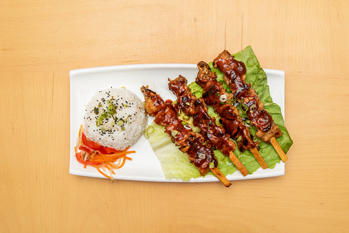 Grilled pork skewers with barbecue sauce, chives, white rice and cooked vegetables for garnish