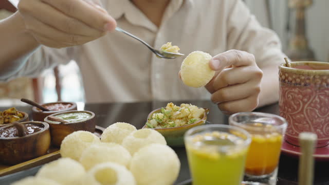 Asian man with eyeglasses preparing pani puri, Indian food and tasting it happily for the first time at the Indian restaurant