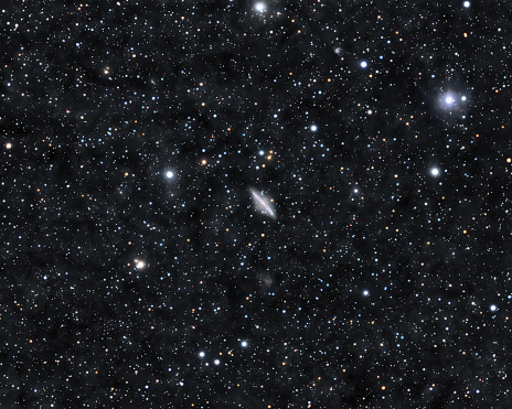 Astronomical image of the galaxy NGC2683 glowing through the dense star field and nebulae of Lynx constellation