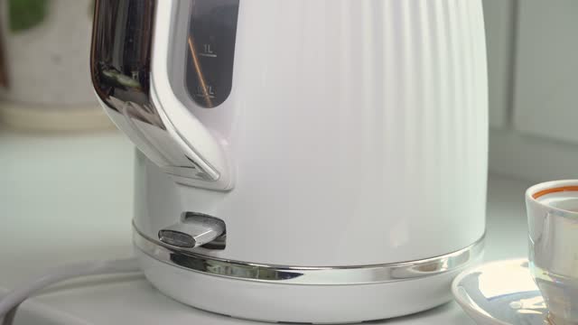 White electric kettle boils water. Turning on the kettle to make tea or coffee in the morning