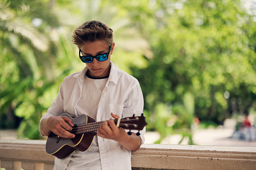 Teenage boy playing ukulele in the public park\nCanon R5
