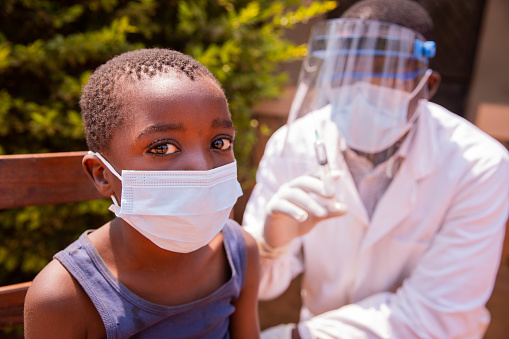 Portrait of a child in a clinic in Africa about to be vaccinated with the doctor beside him