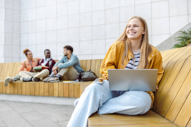 Young female student using laptop on the bench on campus