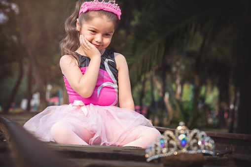 beautiful minor little girl playing in the park with ballerina costume laughing screaming with happiness in family enjoying children's day on train tracks