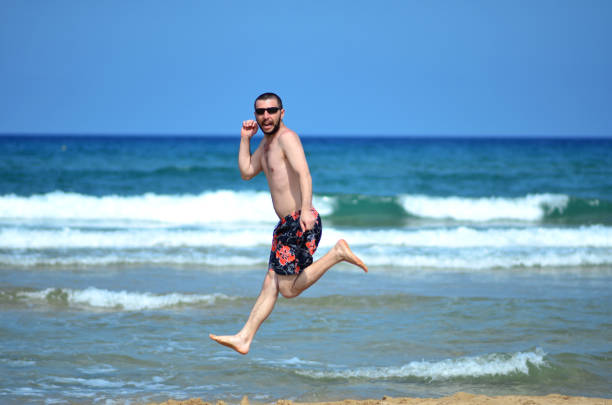 A man jumps on the beach in front of the sea against a blue sky