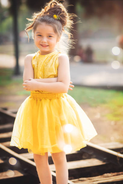beautiful junior little girl playing in the park in yellow dress laughing with bubbles, screaming with happiness in family enjoying children's day stock photo